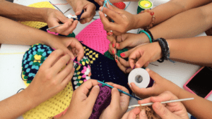 The hands of several people crocheting with yarn and crochet hooks.