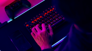 video game controller above a keyboard with a person's hands poised above the keys.