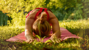 A woman in child's pose on a yoga mat in the grass.
