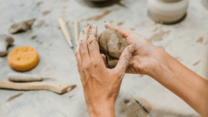 A person holding and sculpting clay with clay tools on the table in the background.